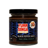 A jar of Yumm Singa black pepper sauce with black, blue and red branding, pictured on a white background