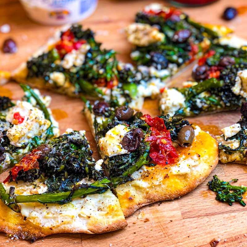 Cooked Pinsa Romana with Purple Sprouting Broccoli, ricotta and olives on a wooden board
