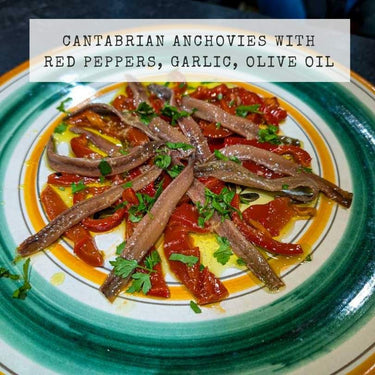 Cantabrian anchovies with red peppers, garlic, and olive oil on a decorative plate.