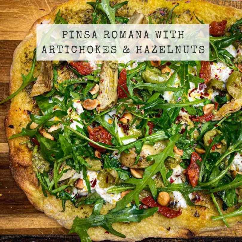 Pinsa Romana with artichokes and hazelnuts on a wooden board