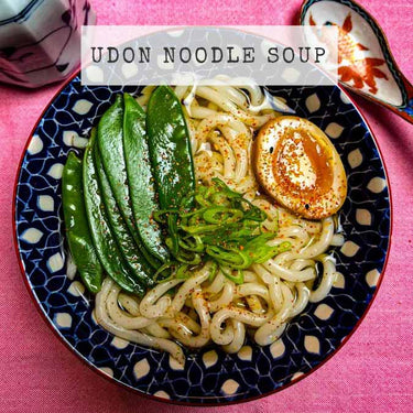 Recipe for Japanese Udon Noodle Soup in a blue bowl with spring onions, egg, mange toute and shichimi togarashi.